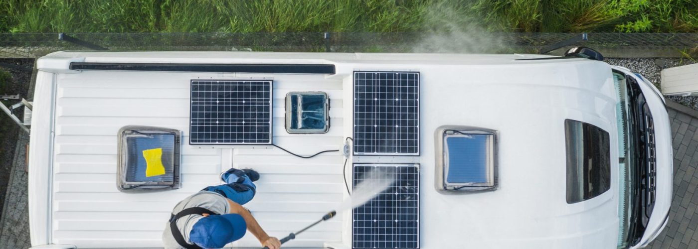 Caucasian Men in His 40s Power Pressure Washing Recreational Vehicle RV Camper Van Roof Equipped with Solar Panels. Camping Pre Season Motorhome Maintenance.